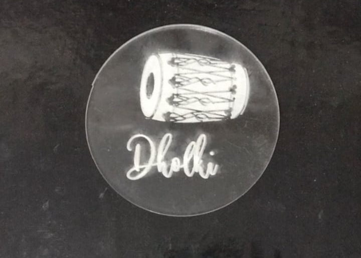 Clear circular sticker with dholki design and 'Dholki' text on a black background